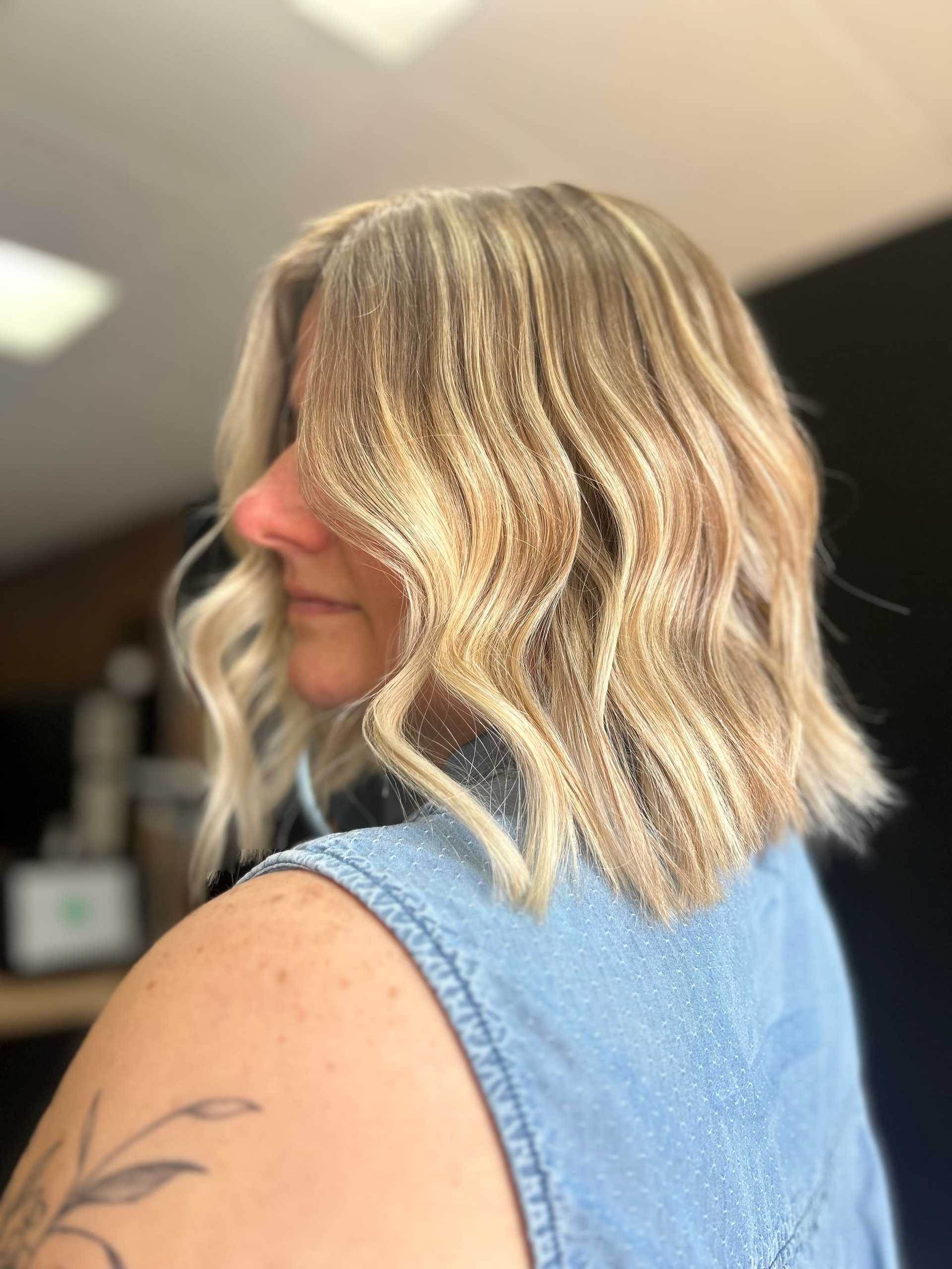 Woman with wavy blonde bob hairstyle in denim shirt, side profile view.