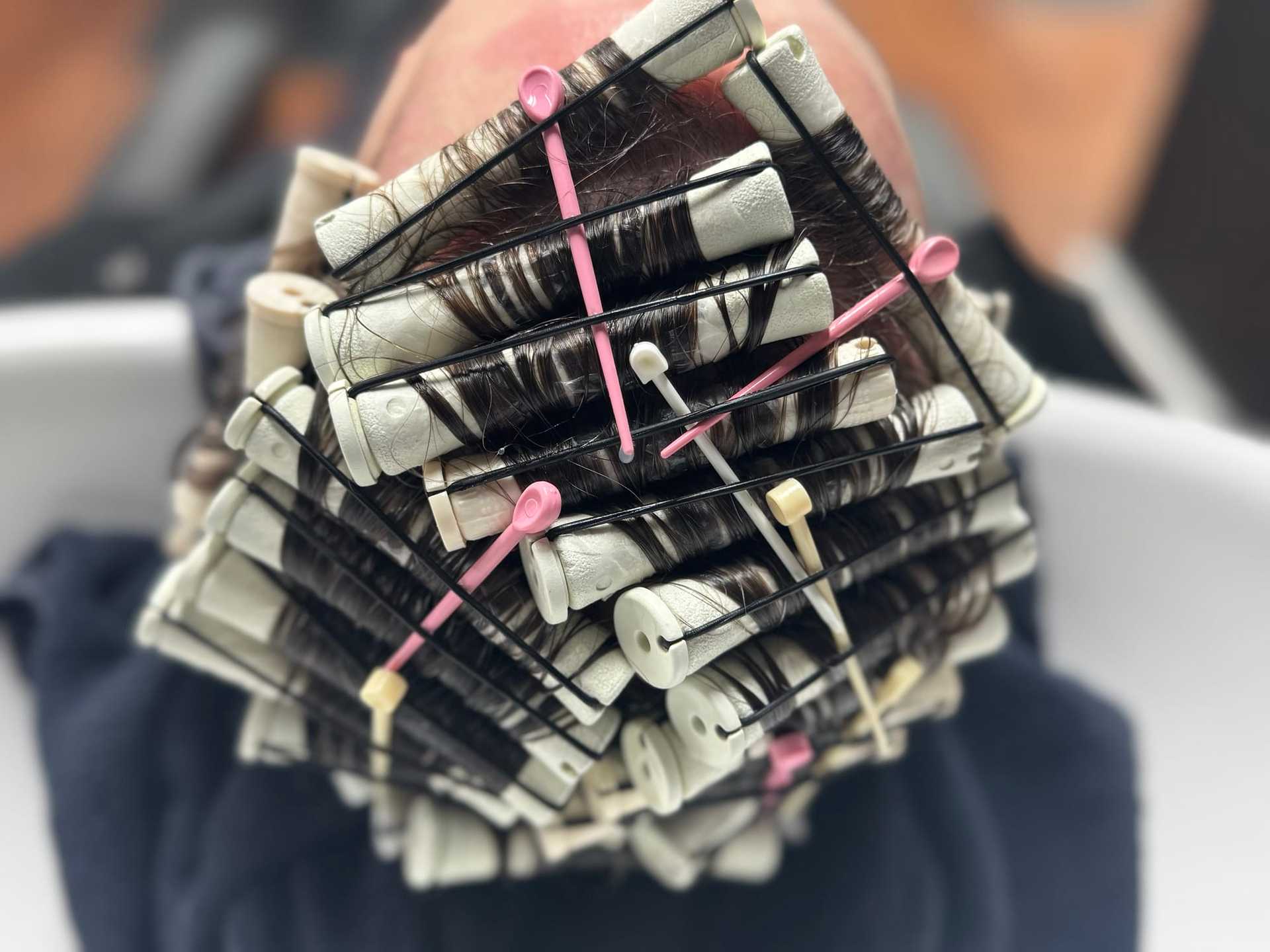 Hair being styled with perm rods and clips, viewed close-up from above, in a salon setting.