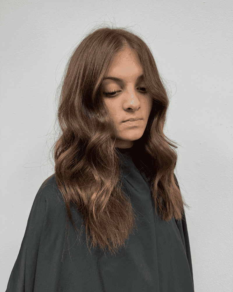 Woman with wavy brown hair wearing a dark cape against a light gray background.